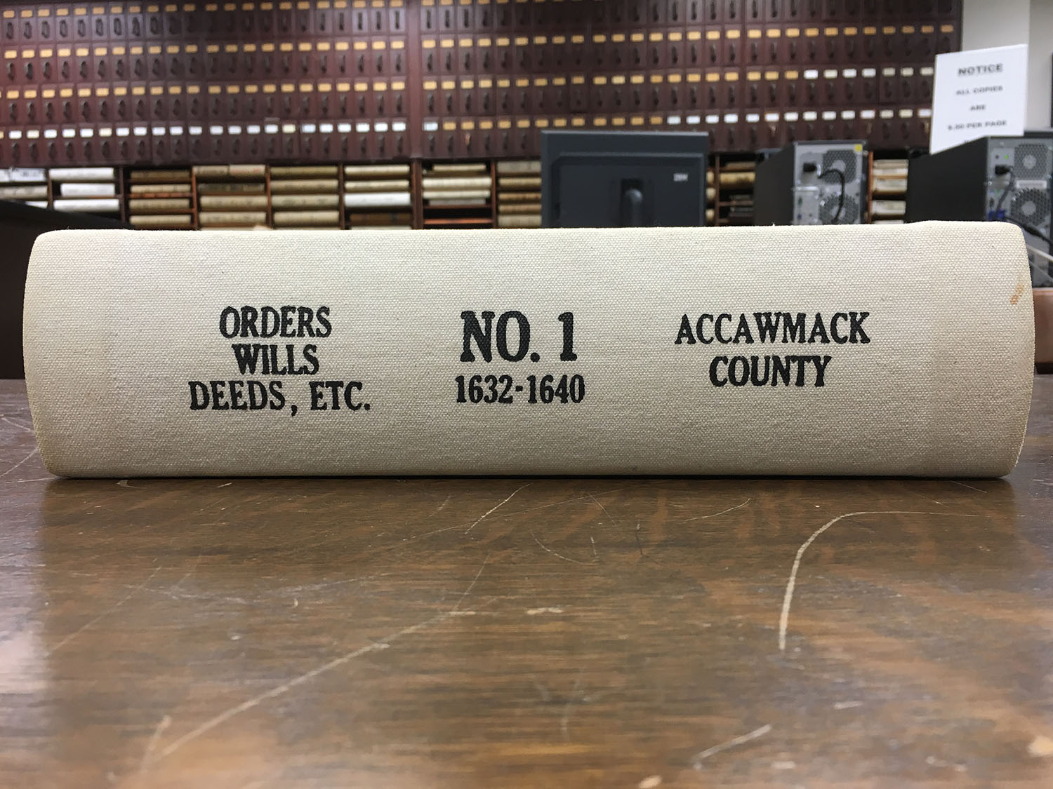 Image shows the spine of a bound volume that says "Orders Wills Dees Etc. No. 1 1632-1640 Accawmack County" sitting on a table.