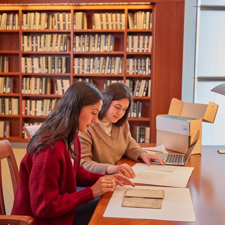 Two women examine historical documents on a table