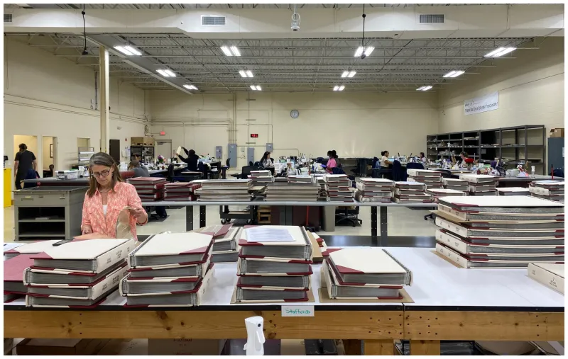 large industrial room, people in the background are conserving records. Women on left inspecting bound conserved volumes.