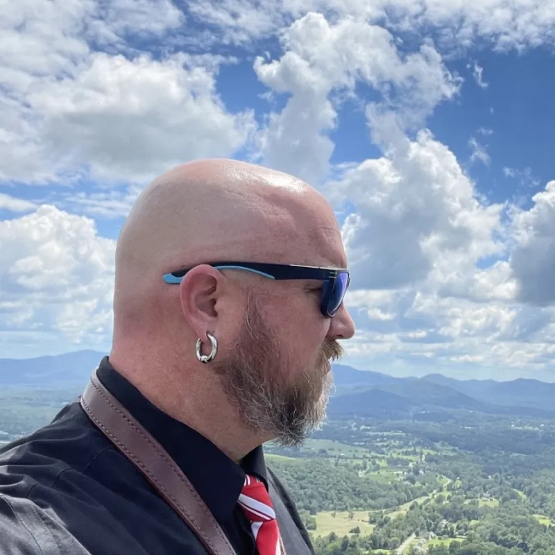Man in black shirt in sunglasses standing in profile. Shenandoah Valley in the background.