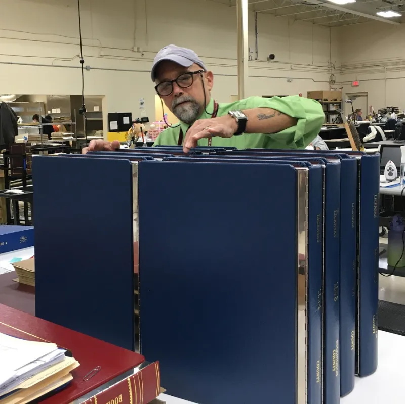 man in gray hat with with glasses and green shirt inspected conserved volumes with blue plastic bindings